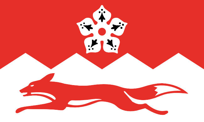 A red above and white below flag split by a zig-zag pattern. The bottom portion has a red fox running, while the top has a white flower with black inner pattern