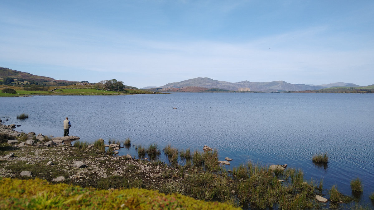 A fisherman on the shore of the lake, the power station in the distance